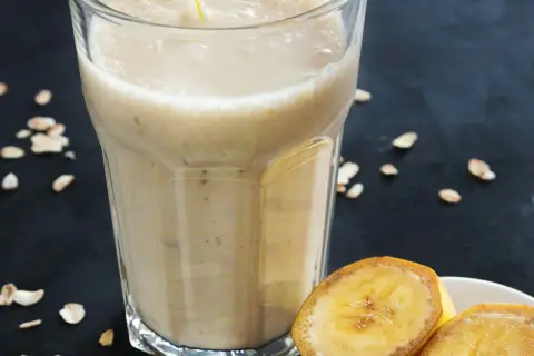 שייק חלבון בננה בכוס גבוהה עם פתיתי שיבולת שועל ובננה חתוכה